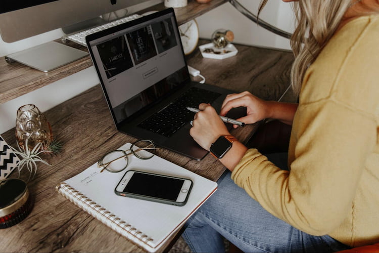 a woman sits at a desk, working on a laptop