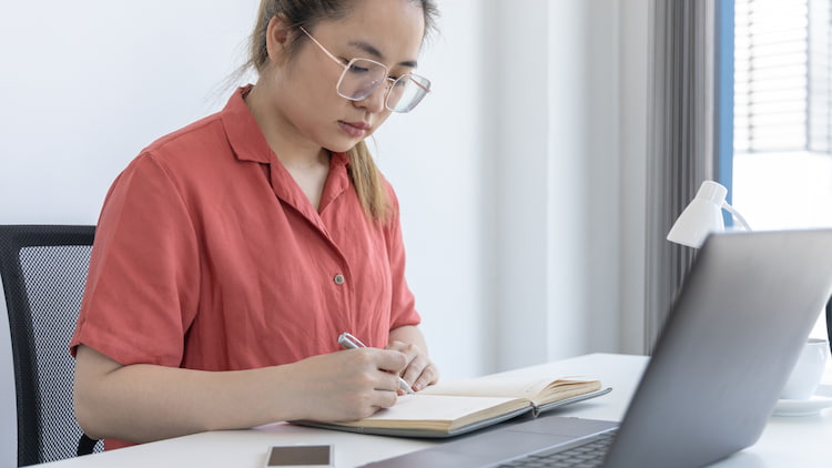 a woman sits at a desk, journaling