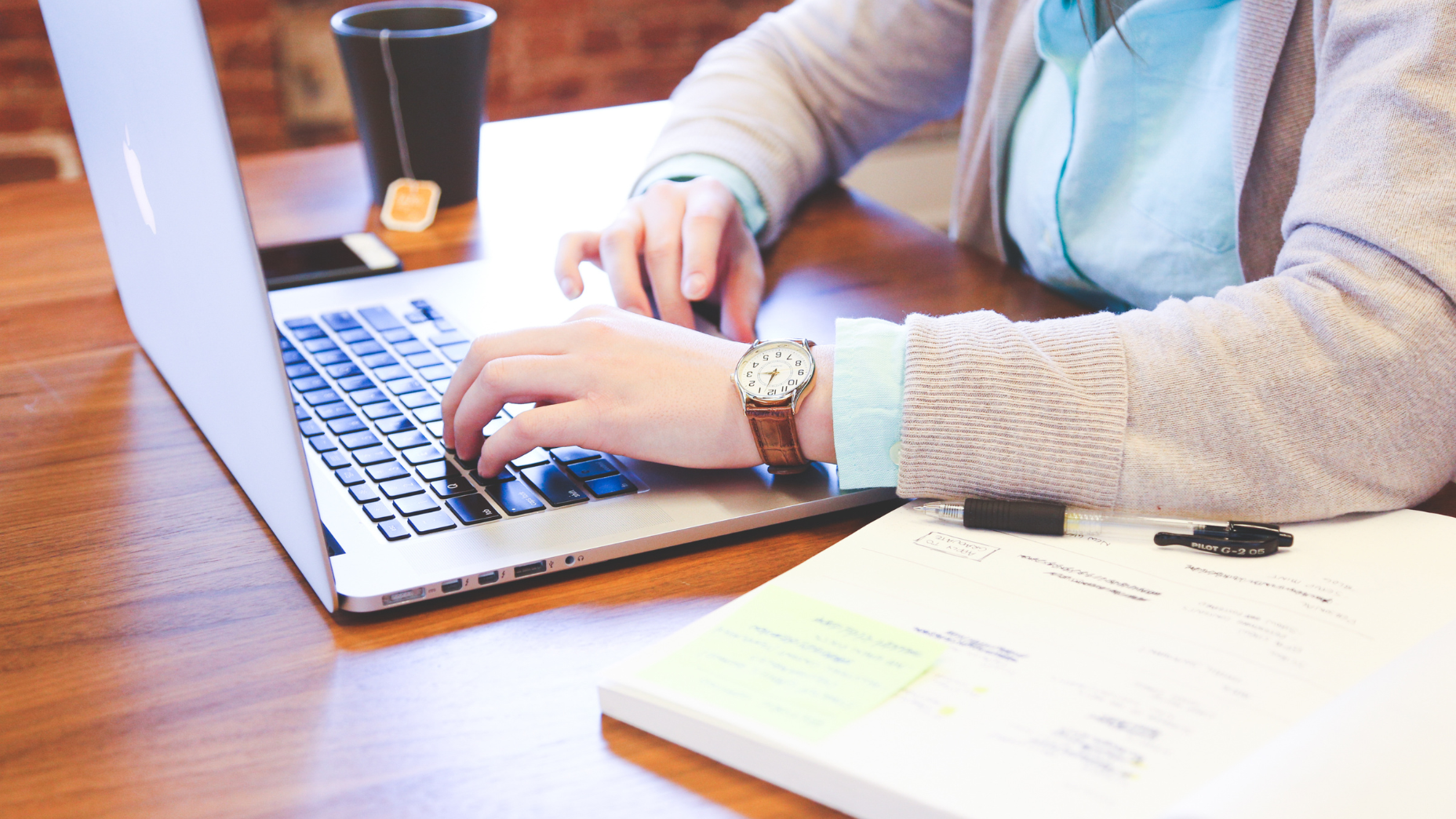 A woman works on a laptop alongside a planner notebook and pen.