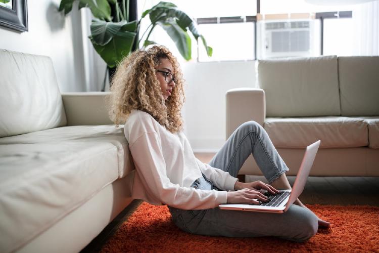 A woman sits on the floor and uses a laptop, perhaps to learn grant writing!